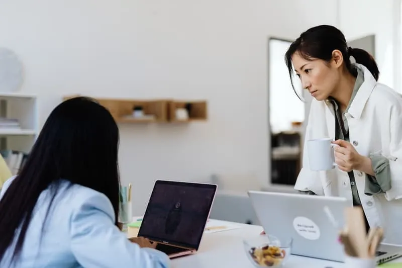 dua orang wanita sedang bekerja di depan laptop