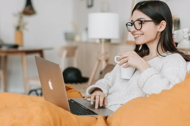 seorang wanita meminum kopi sambil memainkan laptop