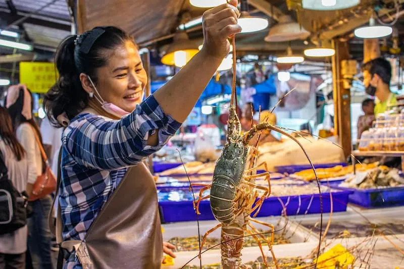 seorang wanita sedang mengangkat lobster sambil tersenyum