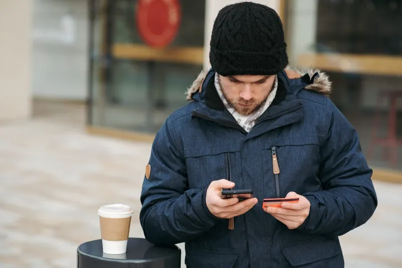 seorang pria memegang handphone dan kartu kredit di jalan